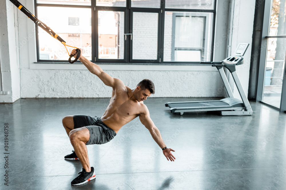 Fototapeta premium handsome sportsman working out on suspension trainer in sports center
