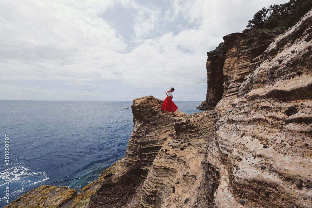 woman traveller wearing red dress on amazing view cliff looking to ocean