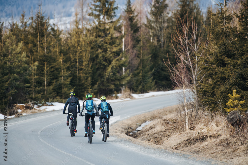 Obraz premium Rear view of mountain bikers riding on road in mountains outdoors in winter.