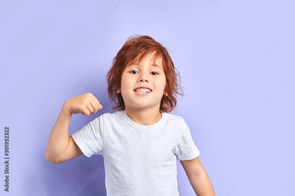 Portrait of caucasian child wearing white t-shirt shows how he is strong and powerful, idolated over purple background Portrait of caucasian child wearing white t-shirt shows how he is strong and powerful, idolated over purple background