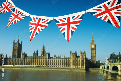 Traditional British Union Jack flag bunting hanging in front of the Westminster Palace in blue sky in London, UK