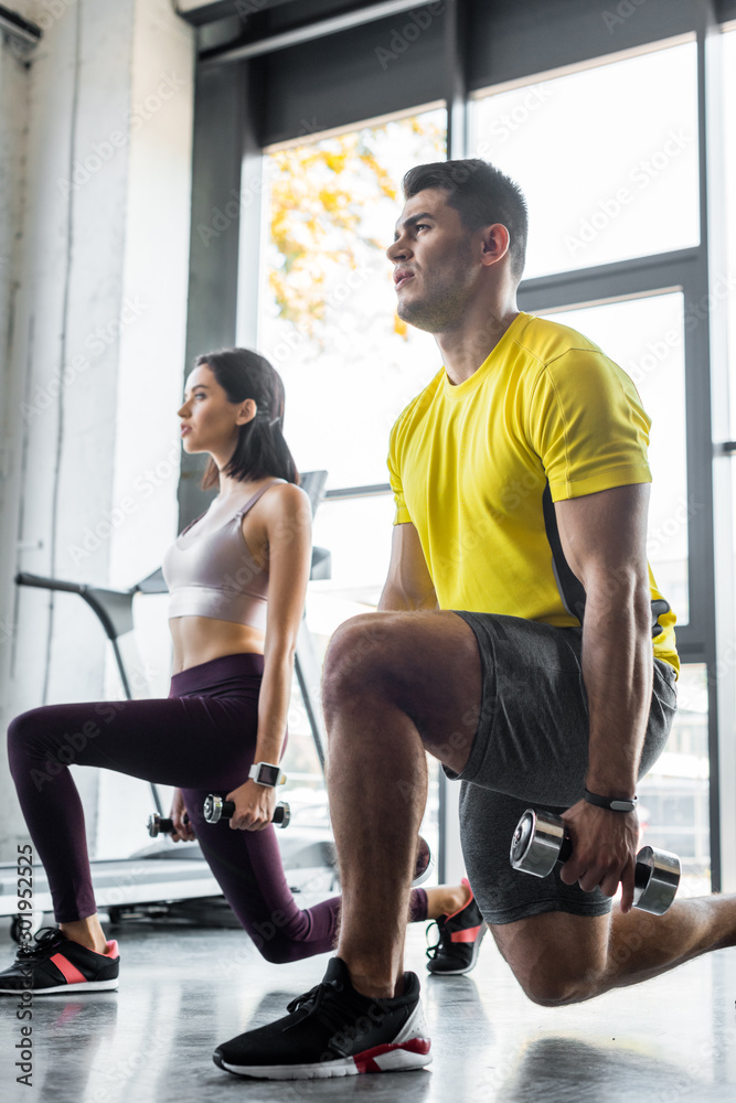 Obraz premium sportsman and sportswoman doing lunges with dumbbells in sports center