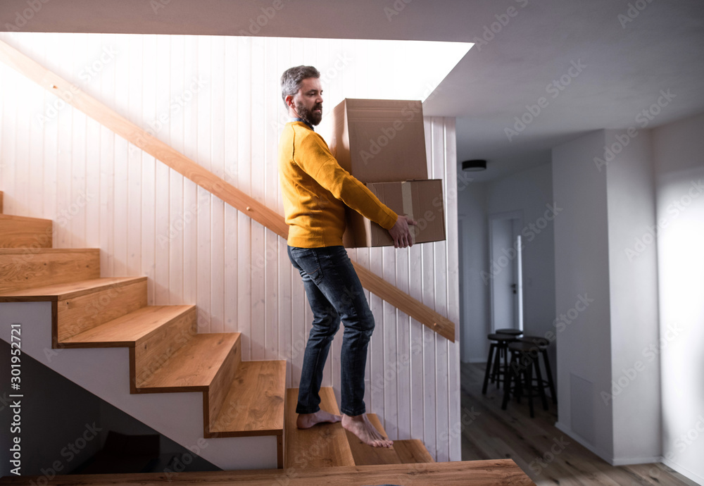 Mature man walking down stairs in house, holding moving boxes.