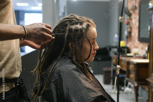 African master hairdresser  making dreadlocks for young woman in hair salon photo