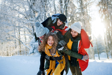 Group of young friends on a walk outdoors in snow in winter forest, having fun.