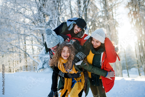 Group of young friends on a walk outdoors in snow in winter forest, having fun.