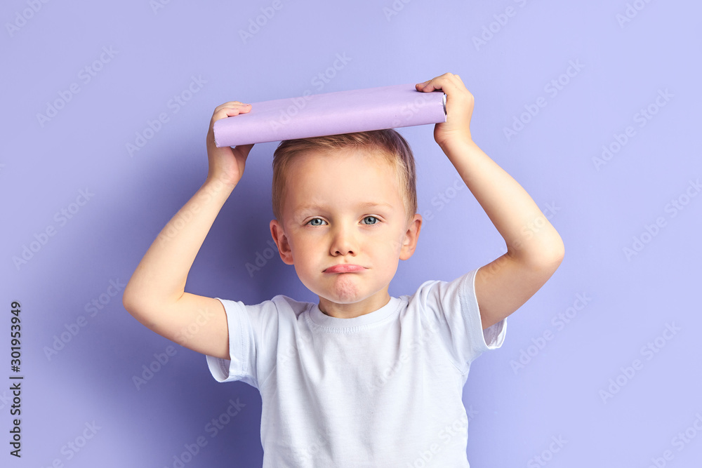 Sad face of child. Caucasian little boy tired of reading book, hold book above head. Kid's expressions of upset and fatigue, isolated purple background Sad face of child. Caucasian little boy tired of reading book, hold book above head. Kid's expressions of upset and fatigue, isolated purple background