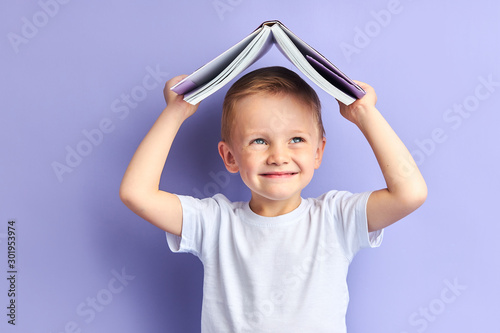 Portrait of joyful caucasian child in casual clothes after education, after reading wants to play. Funny boy holding book above his head