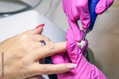 А manicurist in pink gloves processes the nails of an adult client using a variety of equipment. Manicure. Beauty shop. Gloved hands take care of the nails of the hands. Procedures.