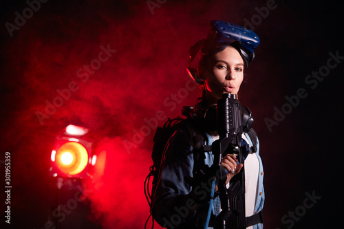 Good-looking female look at camera, holding VR weapon, standing in studio, smoky background