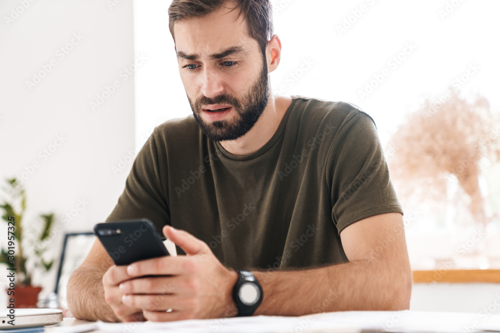 Image of caucasian confused man typing on cellphone while sitting Image of caucasian confused man typing on cellphone while sitting