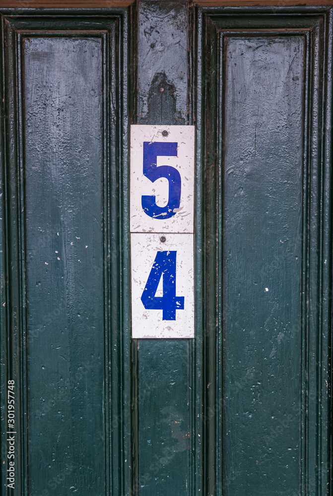 The number 54 is attached to a green pitted wooden door The number 54 is attached to a green pitted wooden door