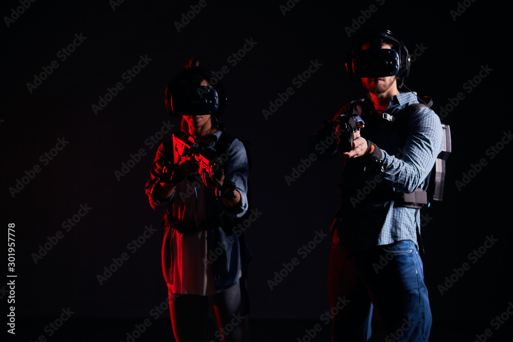 Naklejka premium Youg couple direct their virtual weapons at camera, in search of enemy, virtual war. Futuristic, fantasy, innovation concept