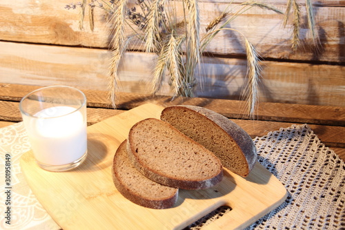 Cut brown bread on wooden board, glass of milk and spicas in rustic style photo