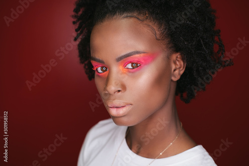Studio portrait of fashion African female model with make up. Red coloured background