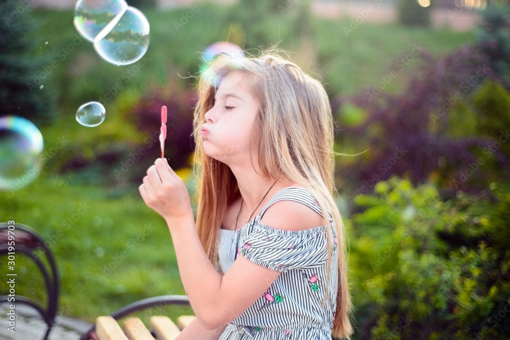 portrait of a beautiful little girl, a child, sitting on a bench, in the park, blowing bubbles. Active lifestyle of children