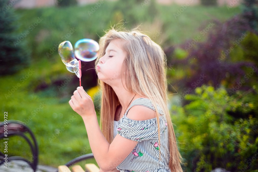 portrait of a beautiful little girl, a child, sitting on a bench, in the park, blowing bubbles. Active lifestyle of children portrait of a beautiful little girl, a child, sitting on a bench, in the park, blowing bubbles. Active lifestyle of children