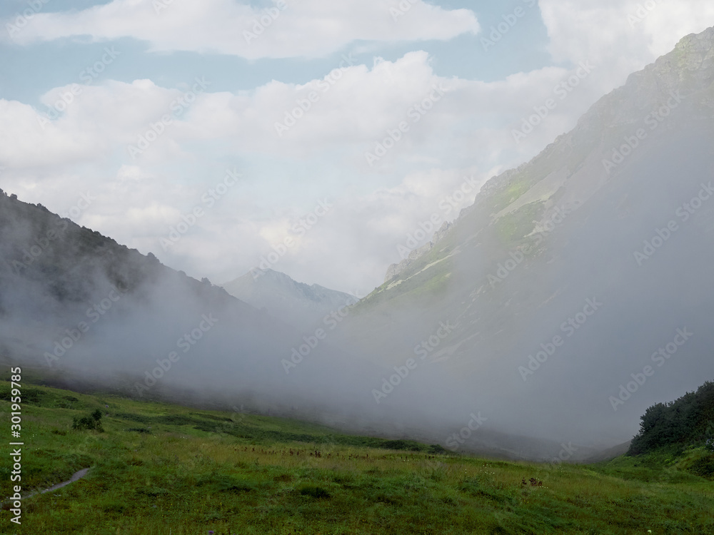 Foggy gorge; clouds floating between mountain ranges; trekking route in nature terrain; mountain trail through mist, Bzerpinskiy karniz, Russia
