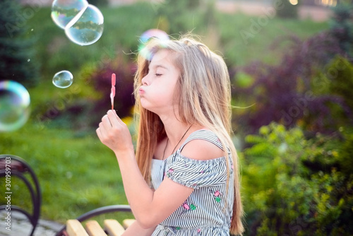 portrait of a beautiful little girl  a child  sitting on a bench  in the park  blowing bubbles. Active lifestyle of children