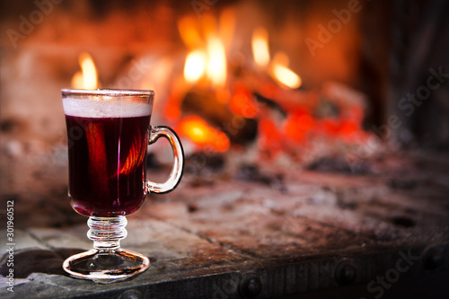 Hot mulled wine in the glass on the background of a burning fireplace. Christmas or winter warming drink.