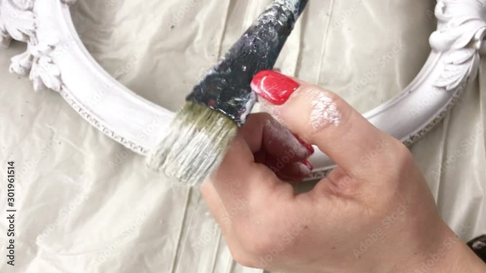 Female hand with a brush smeared with white paint. Woman examines a brush smeared with white paint in a creative lesson on painting frames Female hand with a brush smeared with white paint. Woman examines a brush smeared with white paint in a creative lesson on painting frames