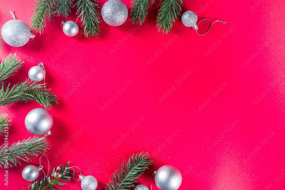Christmas background with fir tree branches and decorations of silver christmas balls. Flat lay on a red background, frame copy space