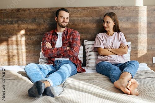 Lovely happy family sitting in bedroom, can not hide smile, ready to make up quarrel, looking at each others, waiting for partner to start talking, optimistic mood, portrait