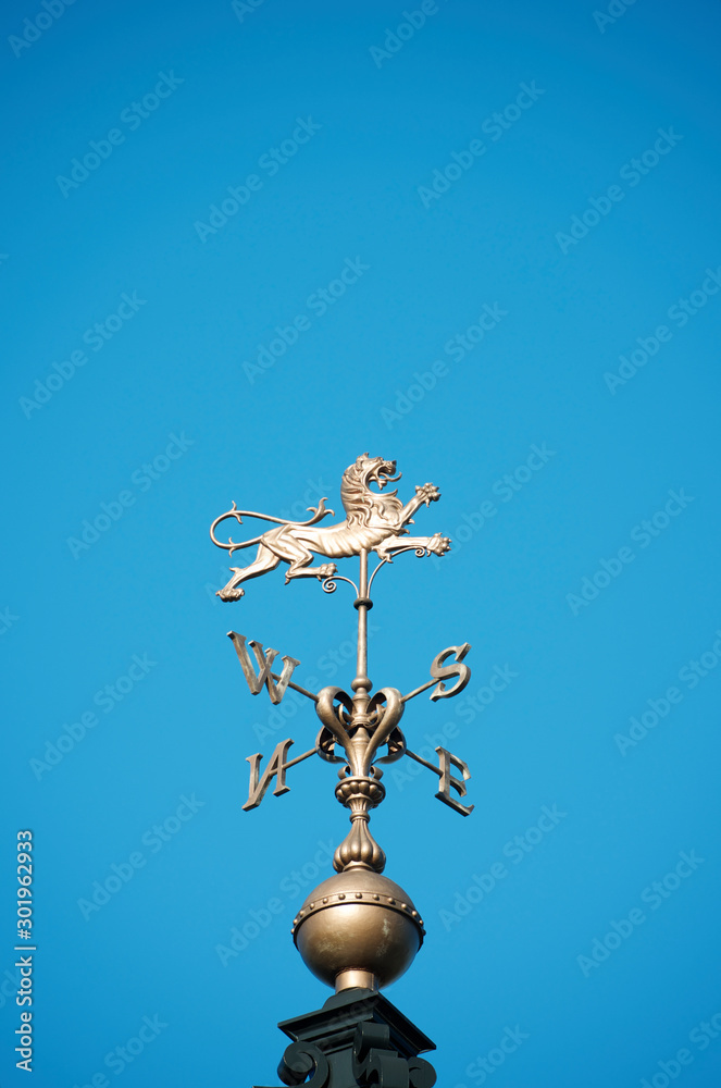 Brass weather vane with fierce lion shining golden in bright blue sky