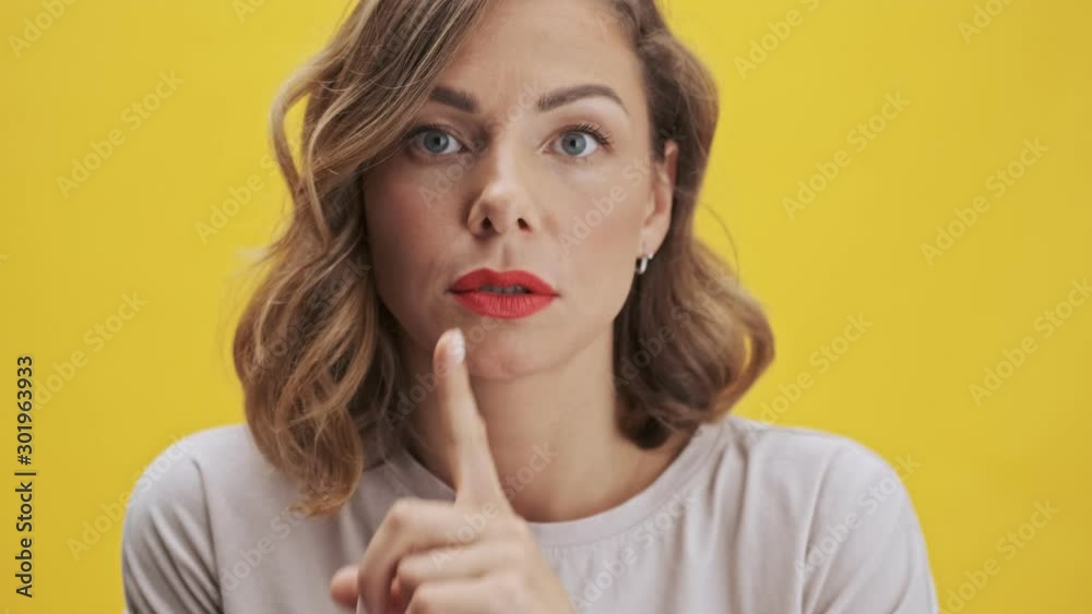 Goodly young woman with red lips making a silence gesture while looking at the camera over yellow background isolated Goodly young woman with red lips making a silence gesture while looking at the camera over yellow background isolated