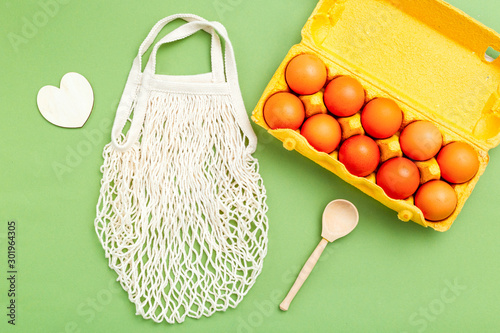 Reusable bag and egg in organic packaging on green background. Zero waste photo