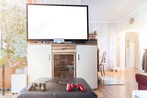 A widescreen TV with Copy Space. In the foreground are joysticks and a game console. Authentic home interior.