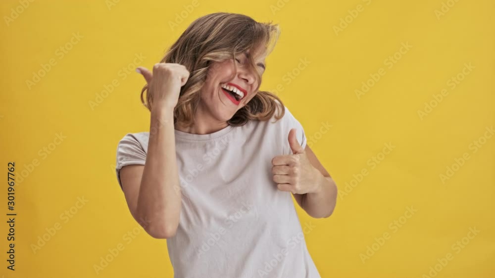 Charming and happy young woman with red lips laughing and dancing over yellow background isolated                                                                          