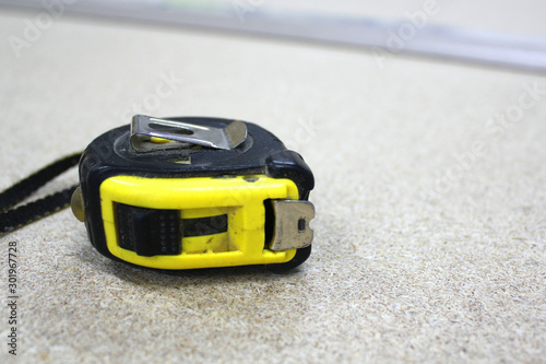 Tape-measure is on the chipboard. Yellow and black tape-measure is on the table.
