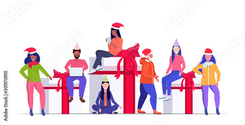 mix race people in santa hats preparing for christmas and new year party celebration men women sitting on gift present boxes winter holidays concept full length horizontal vector illustration