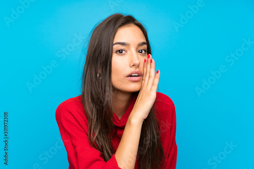 Young woman with red sweater over isolated blue background whispering something