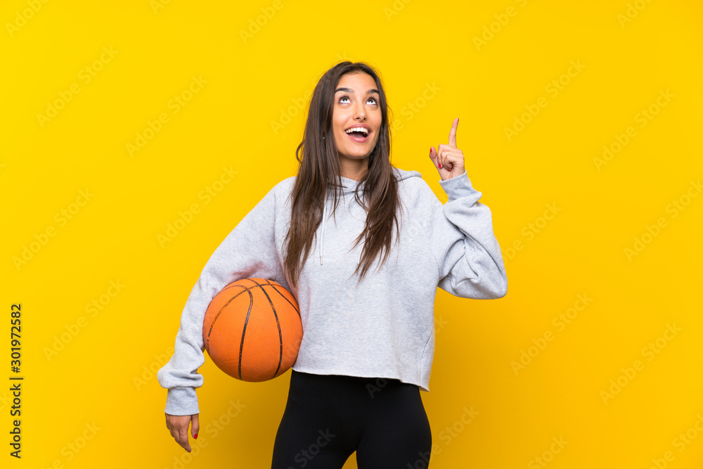 Young woman playing basketball over isolated yellow background intending to realizes the solution while lifting a finger up Young woman playing basketball over isolated yellow background intending to realizes the solution while lifting a finger up