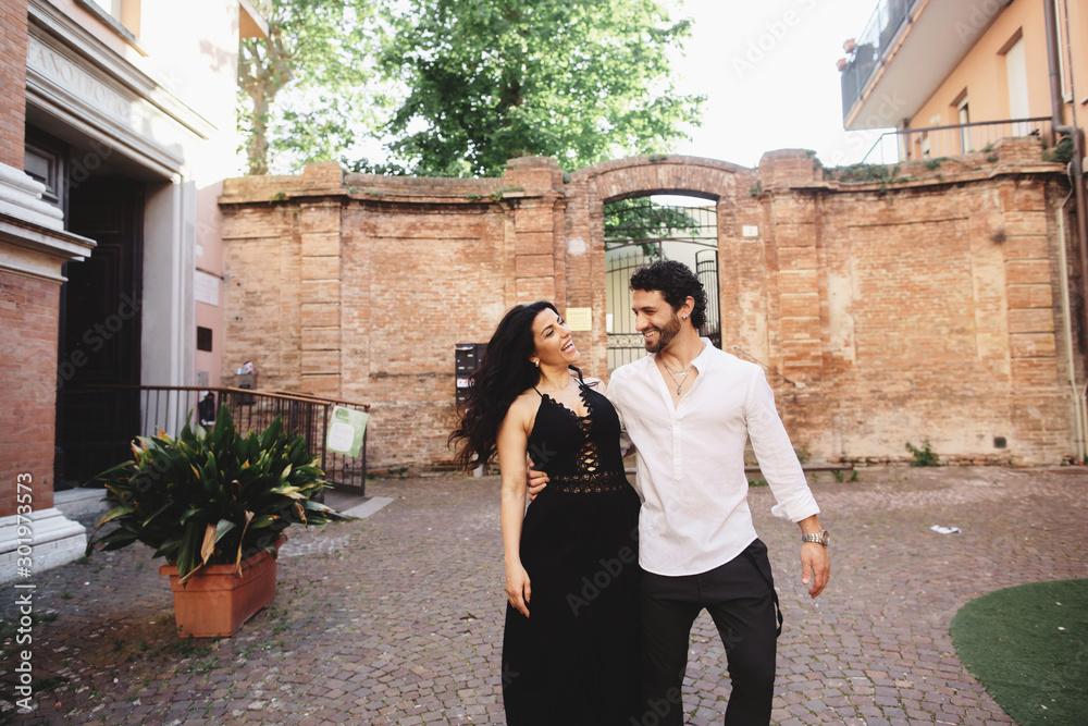 A young love couple enjoying a walk in the courtyard of the old city. Against the background, red brick walls A young love couple enjoying a walk in the courtyard of the old city. Against the background, red brick walls