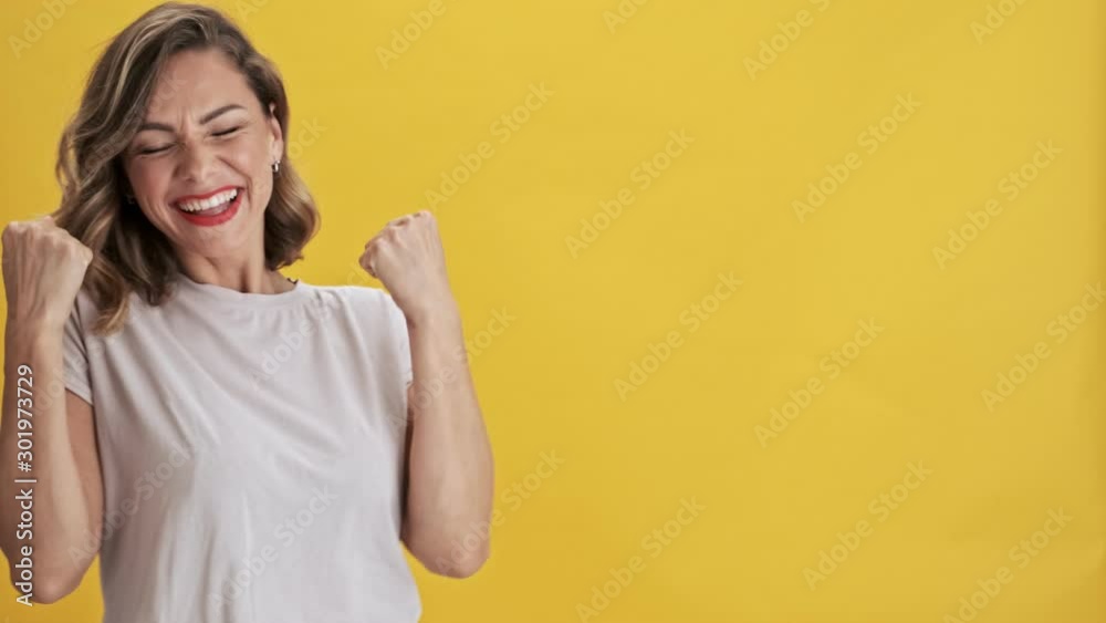 Smiling young woman with red lips showing a winner gesture over yellow background isolated Smiling young woman with red lips showing a winner gesture over yellow background isolated