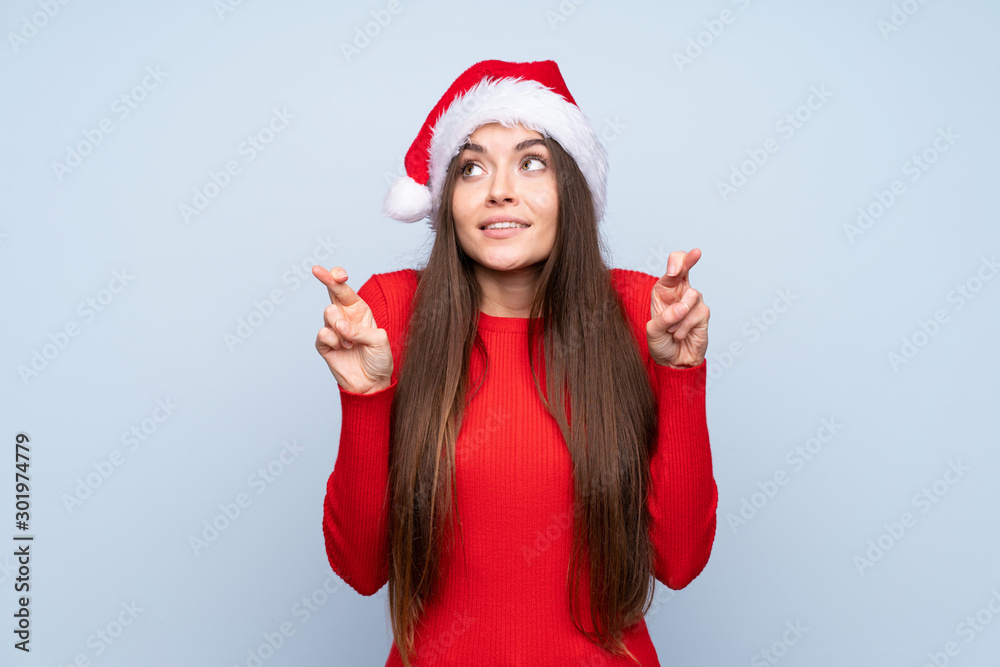 Girl with christmas hat over isolated blue background with fingers crossing Girl with christmas hat over isolated blue background with fingers crossing