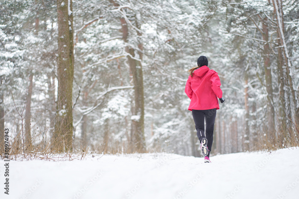 Redhead woman wearing pink sport outfit runing in winter forest, view from back, copy space