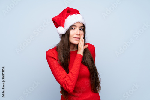 Girl with christmas hat over isolated blue background whispering something