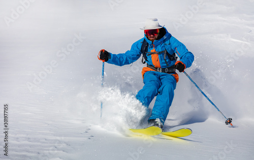 A skier on the slope. Out-of-piste skiing. Good winter day, ski season. professional rider in bright blue-orange ski suit and original hat on his head. high resolution photo quality