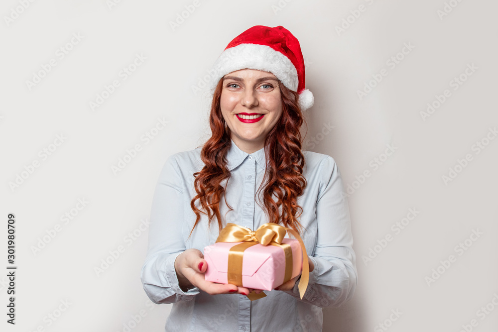 Portrait of a happy girl in a red hat and with lipstick holds a gift box in her hands on a gray background with copy space. Holiday card Portrait of a happy girl in a red hat and with lipstick holds a gift box in her hands on a gray background with copy space. Holiday card