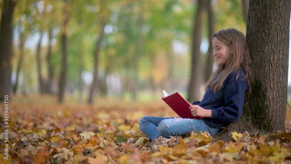 Cute girl reads a book sitting in a park under a tree. Education. Lifestyle Cute girl reads a book sitting in a park under a tree. Education. Lifestyle