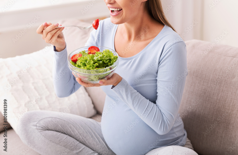 Unrecognizable Pregnant Girl Eating Salad From Bowl Sitting On Sofa