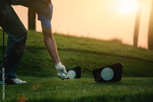 The golfer's hand grips the golf ball and tee presses down at starting point.