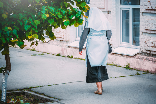 фотографія A nun walks on the sidewalk of an old city