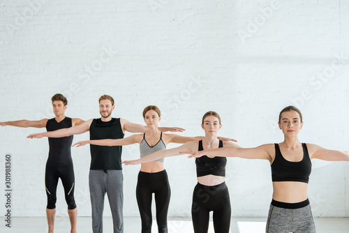 five young men and women practicing yoga in mountain open arm pose