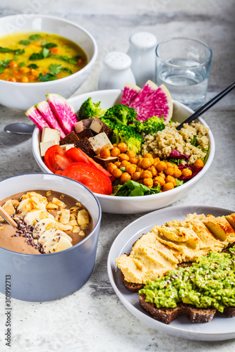 Vegan lunch. Chocolate smoothie bowl, Buddha bowl with tofu, chickpeas and quinoa, lentil soup and toasts on a gray background.