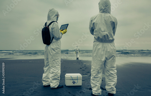 Unrecognizable people with bacteriological protection suits looking for evidence at sea